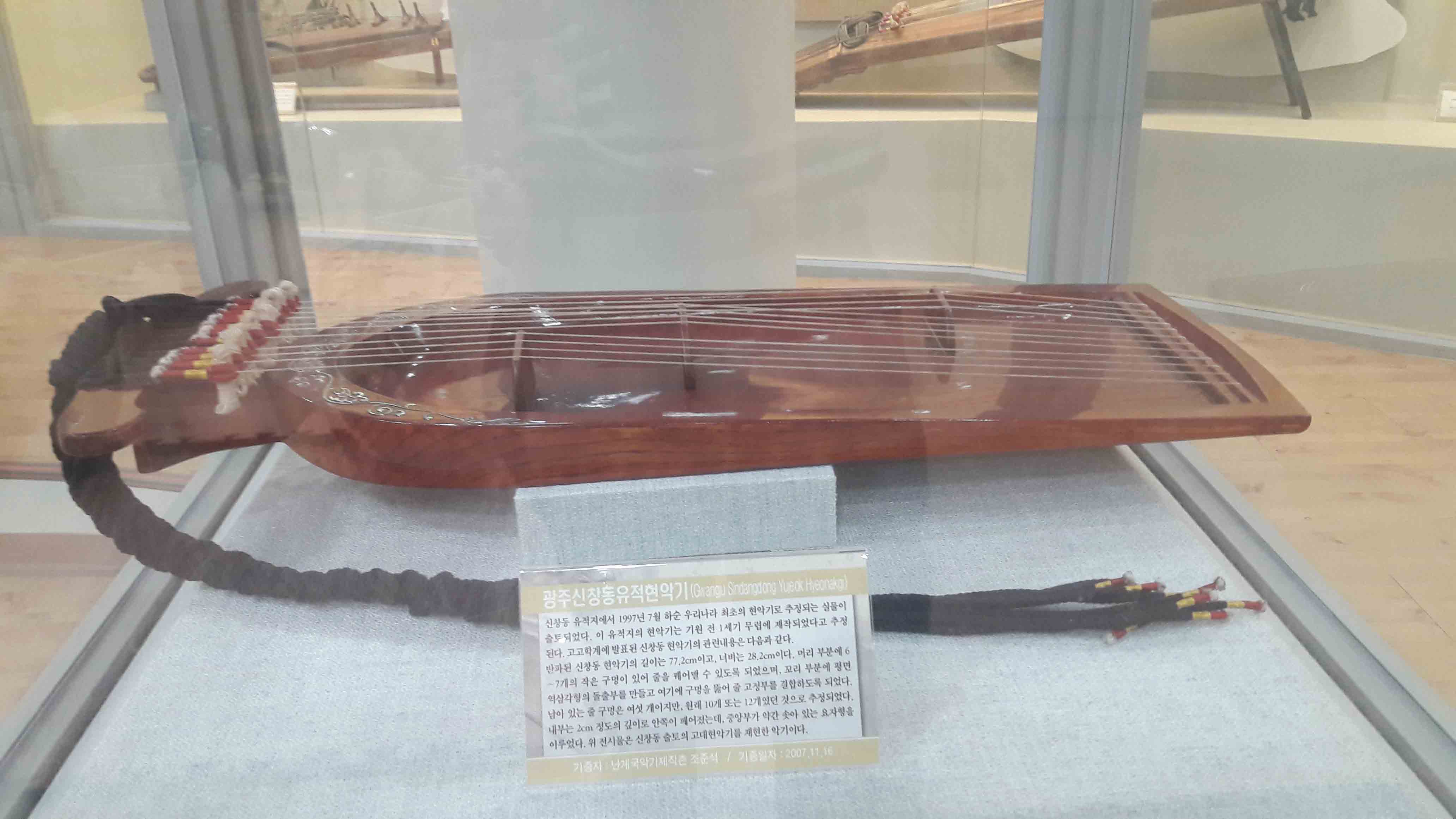광주신창동유적현악기 (Changu Snaanging Yue hieoneto) | 신창동 유적지에서 1997년 7월 하순 우리나라 최초의 현악기로 추정되는 실물이 출토 되었다. 이 유적지의 현악기는 기원 전 1세기 무렵에 제작되었다고 추정 된다. 고고학계에 발표된 신창동 현악기의 관련내용은 다음과 같다. 반파된 신창동 현악기의 길이는 77.2cm이고, 너비는 28.2cm이다. 머리 부분에 6 ~7개의 작은 구멍이 있어 줄을 꿰어맨 수 있도록 되었으며, 꼬리 부분에 핑면 역삼각형의 돌출부를 만들고 여기에 구멍을 뚫어 줄 고정부를 결함이도록 되었다. 남이 있는 줄 구멍은 여섯 개이지만, 원래 10개 또는 12개였던 것으로 추정되었다. 내부는 2cm 정도의 깊이로 안쪽이 끼어있는데, 중앙부가 약간 솟아 있는 요지형을 이루었다. 위 전시물은 신창동 출토의 고대현악기를 재현한 악기이다.