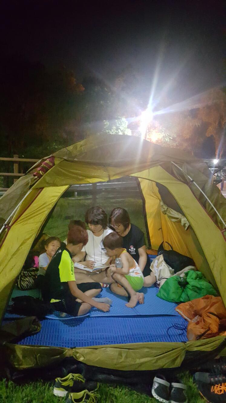 도서관 앞에 텐트를 치고 옹기종기 앉아 책을 읽는 가족 